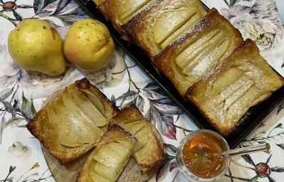 Foto da receita de Folhado de Pera. Observa-se um folhado em forma inglesa com duas peras à esquerda e um potinho de mel na frente,