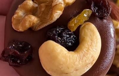 Fotografia em tons de marrom com várias moedinhas de chocolate ao centro enfeitadas com frutas secas, nozes e castanha de caju Fotografia em tons de marrom com várias moedinhas de chocolate ao centro enfeitadas com frutas secas, nozes e castanha de caju