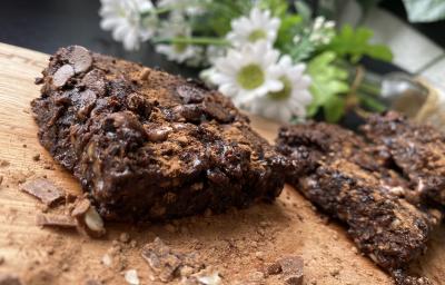 Imagem da receita de Brownie Rápido de Chocolate com Aveia sobre uma mesa e atrás umas flores