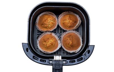 Fotografia vista de cima de quatro muffins de banana sem glúten dentro da cestinha da air fryer, a qual está sobre um fundo branco.