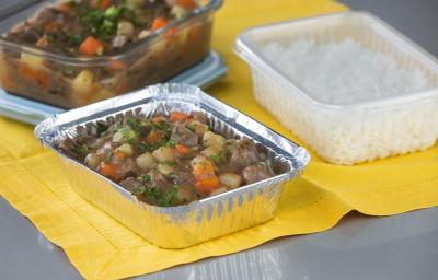 Foto da receita de picadinho de carne, servido em um recipiente de alumínio, sobre uma toalha amarela e acompanhado de arroz num pote de plástico