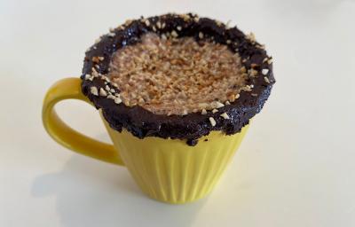 Foto em tons de amarelo da receita de shake de nescau energizante com amendoim servida em uma caneca amarela com cobertura de pasta de nescau e amendoim sobre uma mesa branca