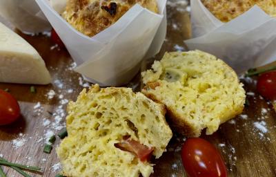 Foto da Receita de Muffin de Pizza. Observa-se um muffin cortado ao meio em cima de uma tábua de madeira. Tomates cereja e queijo decoram a foto também