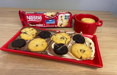 Fotografia de uma barra de chocolate mesclada com chocolate branco, sobre ela uma mistura de biscoitos e cookies.