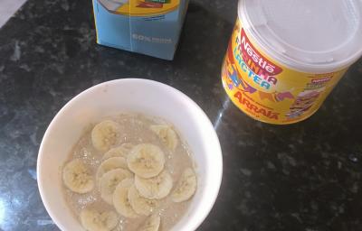 Fotografia de um recipiente branco fundo com um creme de farinha láctea com banana fatiada sobre uma bancada preta.