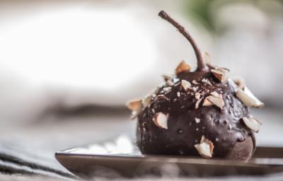 Fotografia de uma pera coberta com chocolate à base de Neston e lascas de nozes sobre um prato de vidro de cor clara.