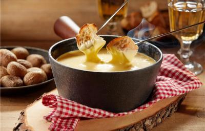 Fotografia mostra um creme brilhante com textura aveludada, servido em aparelho de fondue de cerâmica, acompanhado de cubos de pão dourados mergulhado Fotografia mostra um creme brilhante com textura aveludada, servido em aparelho de fondue de cerâmica, acompanhado de cubos de pão dourados mergulhado