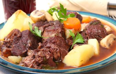 Fotografia com um prato branco e bordas na cor azul. Dentro, um cozido de carne, batata, cenoura e champignon, com folhas de salsinha por cima.