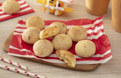 Fotografia em tons de vermelho com vários pães de queijo feitos com NINHO Primeira Infância ao centro.