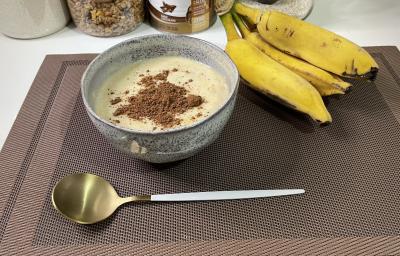 Imagem da receita de Mingau Proteico em um bowl, sobre uma mesa e ao lado uma banana e colher