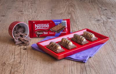 Fotografia mostra quatro barrinhas de chocolate com biscoitos, cobertas com um creme branco e decorada com chocolate derretido.