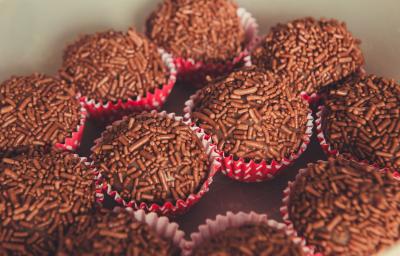 Fotografia de várias unidades de brigadeiro, passados no granulado dentro de forminhas vermelhas com bolinhas brancas.