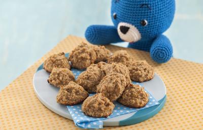 Fotografia em tons de marrom em uma bancada de madeira de cor laranja. Ao centro, há um prato azul contendo os cookies e ao lado, há um ursinho azul sentado.