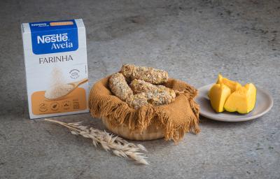 Foto receita de Croquete Vegetariano, servidos em uma cesta de vime, sobre uma bancada de mármore onde há uma caixa de nestlé farinha de aveia à esquerda e pedaços de abóbora sobre um prato à direita além de um ramo de trigo à frente