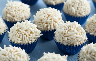 Fotografia em tons de branco e azul de vários brigadeiros em forminhas azuis metalizadas com granulado branco.