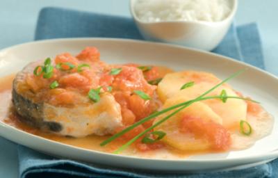 Fotografia em tons de azul e laranja, ao centro um pano azul e acima dele um prato branco com pedaços de peixe e ao lado um potinho com arroz.