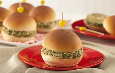 A foto contém diversos pães com hamburguês e palitos com uma bolinha amarela por cima. Um prato vermelho com um pão com hambúrguer à frente