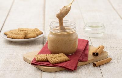 Foto da receita de Pasta de Tostines Especiarias. Observa-se um pote de vidro com a pasta e uma colher mostrando a cremosidade. Biscoitos TOSTINES e canelas em pau decoram a foto.