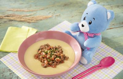 Foto da receita de Polenta Mole com Molho de Carne Moída. Observa-se um potinho rosa bebê com a polenta e a carne dentro, sobre um paninho quadriculado colorido. O ursinho Bo está do lado direito.