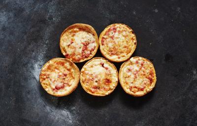 Fotografia vista de cima de cinco mini pizzas de mozarela sobre uma bancada preta com um pouco de farinha.