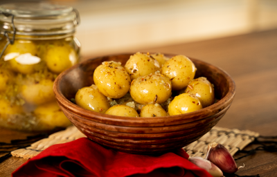 Foto da receita de Batata Bolinha em Conserva. Na foto, observa-se as batatas em um recipiente redondo e, a fundo, um pote hermético transparente com as batatas na conserva.