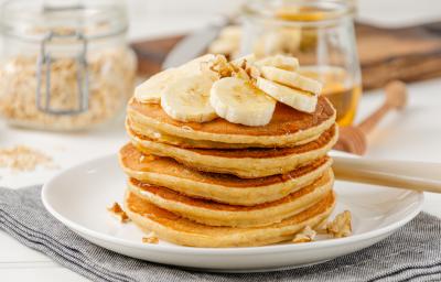 Foto da receita de Panqueca de Banana. Observa-se uma torre de panquecas altas e fofas com banana em cima e um pouco de mel escorrendo.