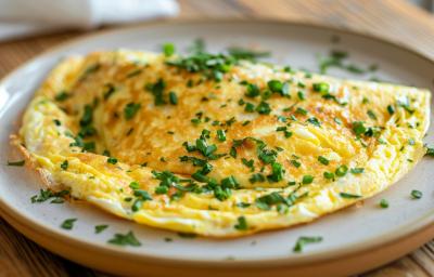 Fotografia de uma omelete rápida sobre um prato de vidro raso, e por cima da omelete tem cebolinha picada salpicada. O prato está sobre uma mesa de madeira.