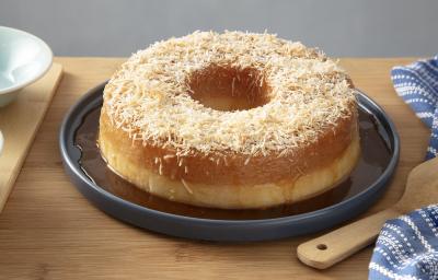 Foto da receita de pudim de tapioca com calda de coco queimado servido em uma porção grande sobre um prato azul escuro em cima de uma mesa de madeira com um paninho azul listrado