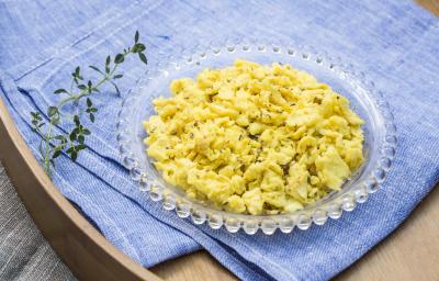 Fotografia em tons de azul e amarelo de uma bandeja de madeira com um pano azul dobrado, sobre ele um ramo de orégano e um pratinho com ovos mexidos.