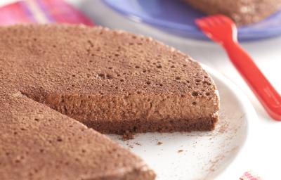 fotografia em tons de azul e marrom tirada de uma torta de chocolate com uma fatia retirada, e ao fundo um prato redondo azul com um pedaço da torta