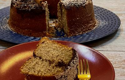 Foto da receita de Bolo com Farofa de Canela. Observa-se um prato de sobremesa com uma fatia do bolo e um garfinho e, atrás, o bolo maior em um prato grande azul.