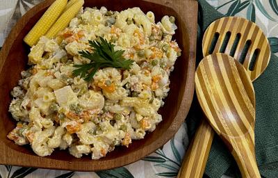 Foto da Receita de Macarronese. Observa-se um recipiente de madeira escuro com a macarronese. Ao lado direito, duas colheres grandes de servir.