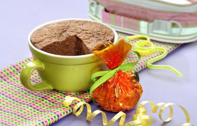 fotografia em tons de cinza, marrom e verde de uma bancada cinza vista de frente, contém um pano em tons de verde, rosa e roxo e uma xicara verde com bolo de chocolate dentro.