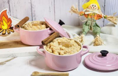 Foto de uma cena com dois potes rosas com a canjica de doce de leite dentro, alguns paus e canela decorado, pequenos espantalhos decorativos ao fundo, tudo sobre uma bancada de mármore branca com tecidos