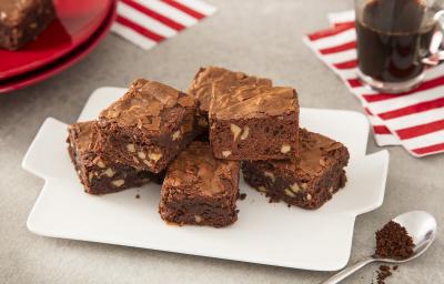 Foto da receita de Brownie de Café. Observa-se 5 pedaços de brownie dispostos um em cima do outro sobre um prato branco. Ao lado direito, uma xícara de café para acompanhar.