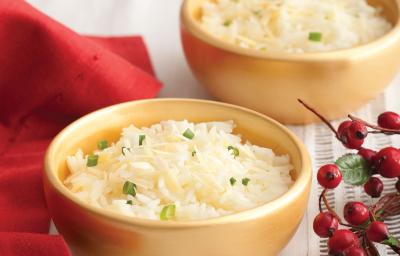 Fotografia em tons de vermelho em uma mesa de madeira com uma toalha branca e um pano vermelho ao lado. Ao centro, um prato fundo dourado com o arroz feito com vinho branco.