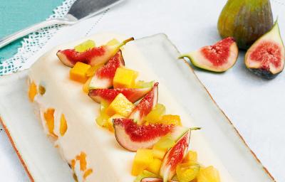 Fotografia em tons de branco e azul claro de uma bancada vista de cima, contém um pano branco, uma travessa branca retangular que contém a sobremesa de gelatina com diversas frutas por cima para decorar.