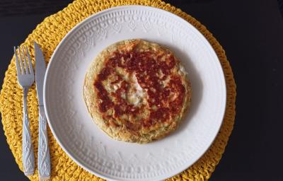 Imagem da receita de Pão de Queijo de Frigideira com Crostinha, em um prato branco, e ao lado os talheres