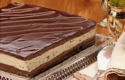 fotografia em tons de marrom de uma bancada marrom vista de frente, em um suporte de alumínio contém a torta com camadas de mousse e chocolate por cima.