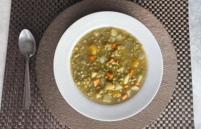 Imagem da receita de Sopa de Ervilha com Legumes, em um prato branco, sobre uma mesa e ao lado uma colher