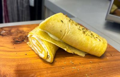 Fotografia em tons de amarelo com uma tábua de madeira ao centro. Em cima da tábua existe uma crepioca recheada com creme de ricota e Ninho Adulto