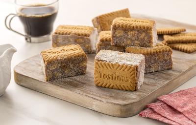 Fotografia de uma tábua de madeira com sete unidades de palha italiana com tostines especiais, ao lado de três biscoitos tostines. No fundo tem uma xícara de vidro com café.