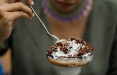 Fotografia de uma pessoa segurando uma colher de sopa e comendo uma sobremesa de camadas de massa e MOÇA Leite Condensado Cremoso. O doce está em uma tacinha de vidro.