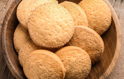 Imagem de pequenos biscoitinhos dispostos sobre um prato fundo de madeira, tons de dourado, amarelo e marrom.