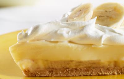 Fotografia de uma fatia de torta de mousse de banana, merengue e rodelas de banana por cima sobre um prato amarelo.