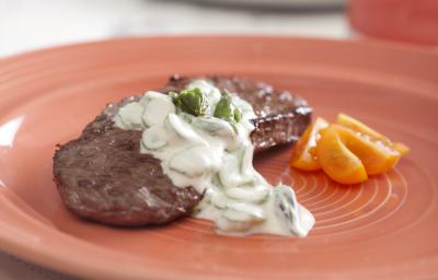 Um prato redondo e rosa visto de frente contém um pedaço de carne com molho branco por cima.