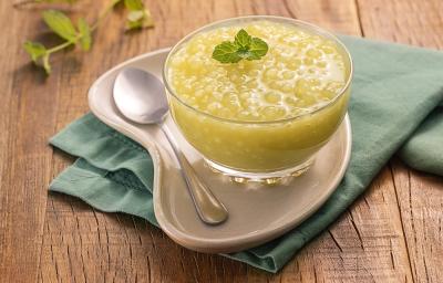 Foto da receita de Sagu Suco Verde. Observa-se uma taça transparente contendo o sagu sobre um prato e um guardanapo verde . Ao lado, uma colherinha e um ramo de hortelã.