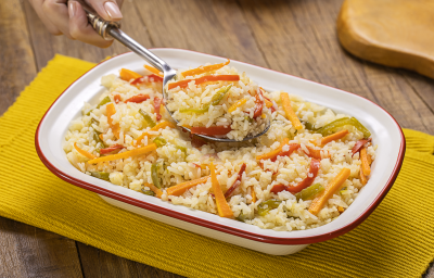 Fotografia mostra uma travessa com arroz com pimentões coloridos e uma colher servindo arroz.