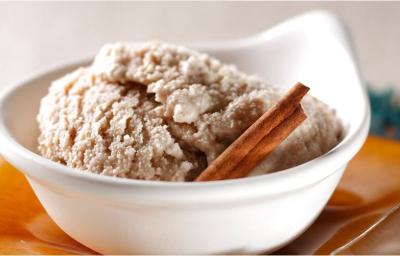 Fotografia em tons de laranja em uma mesa com toalha laranja, um potinho branco com o sorvete de canela, cravo e creme de leite.