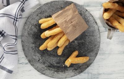 Fotografia em tons de azul em uma bancada de madeira azul mesclada, um pano branco com listras azuis, um prato redondo cinza com vários biscoitos de polvilho fritos. Ao lado, uma caneca com mais biscoitos dentro.